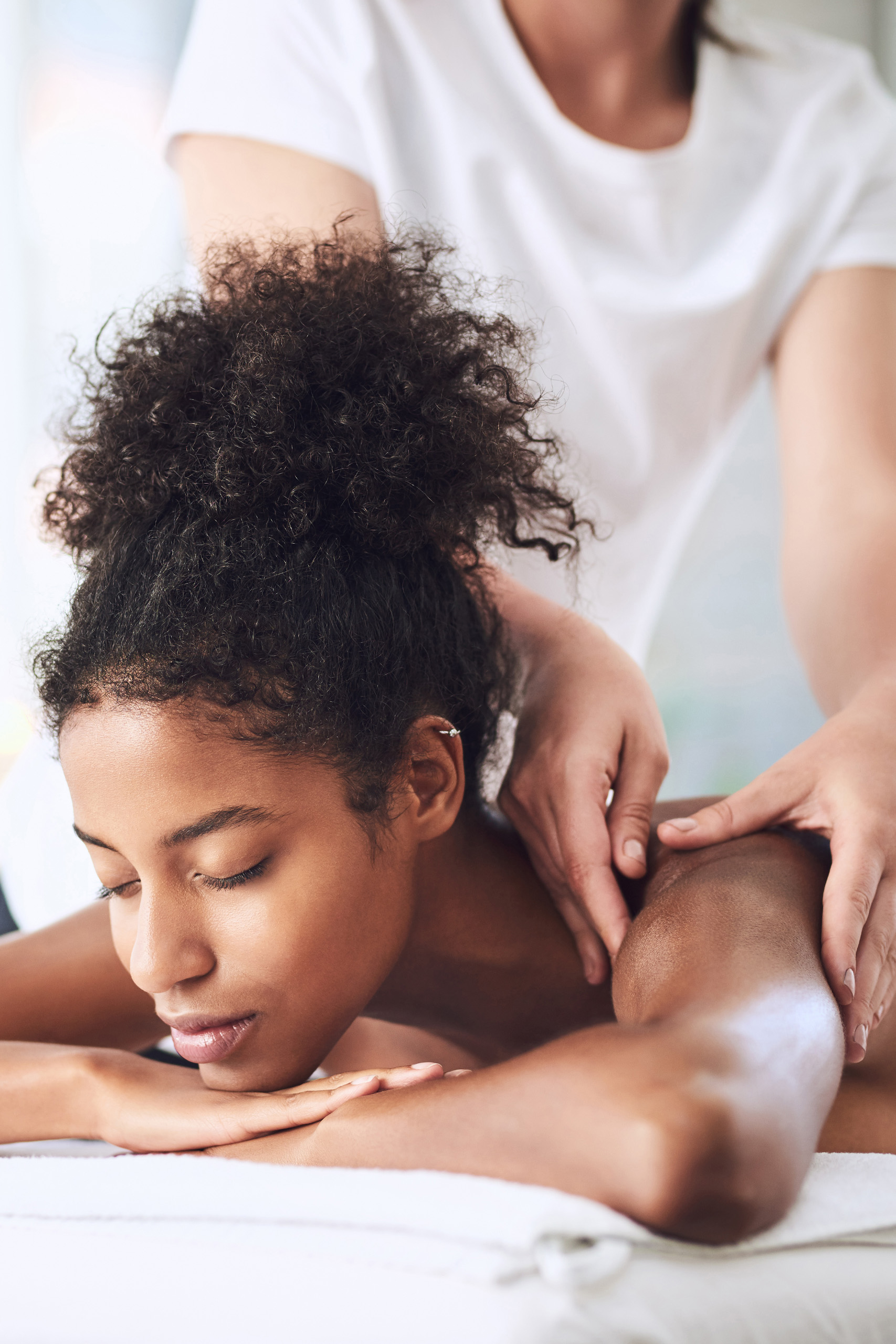 Relaxed BIPOC woman with a pony-tail getting a professional massage.