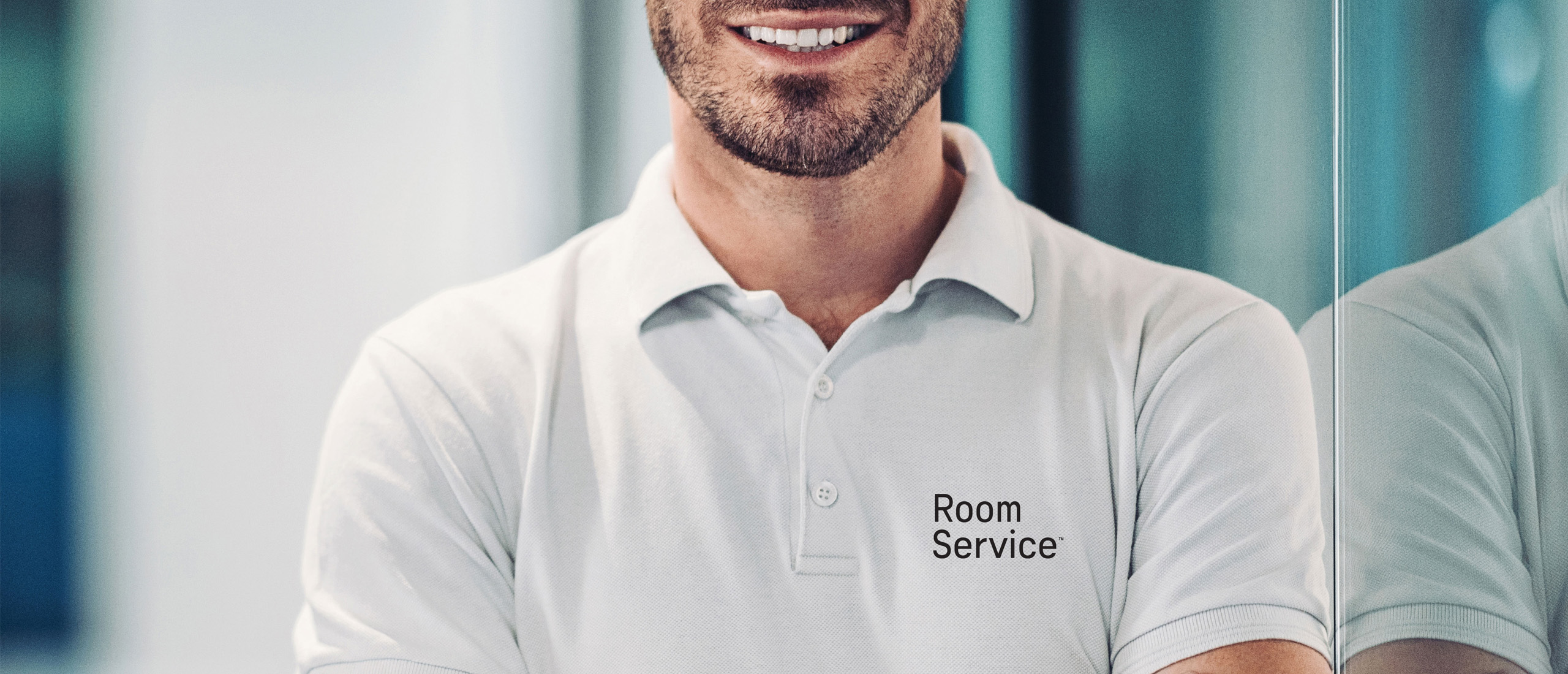 Undistinguishable man with facial hair wearing a light polo shirt with the Room Service logo on the left side